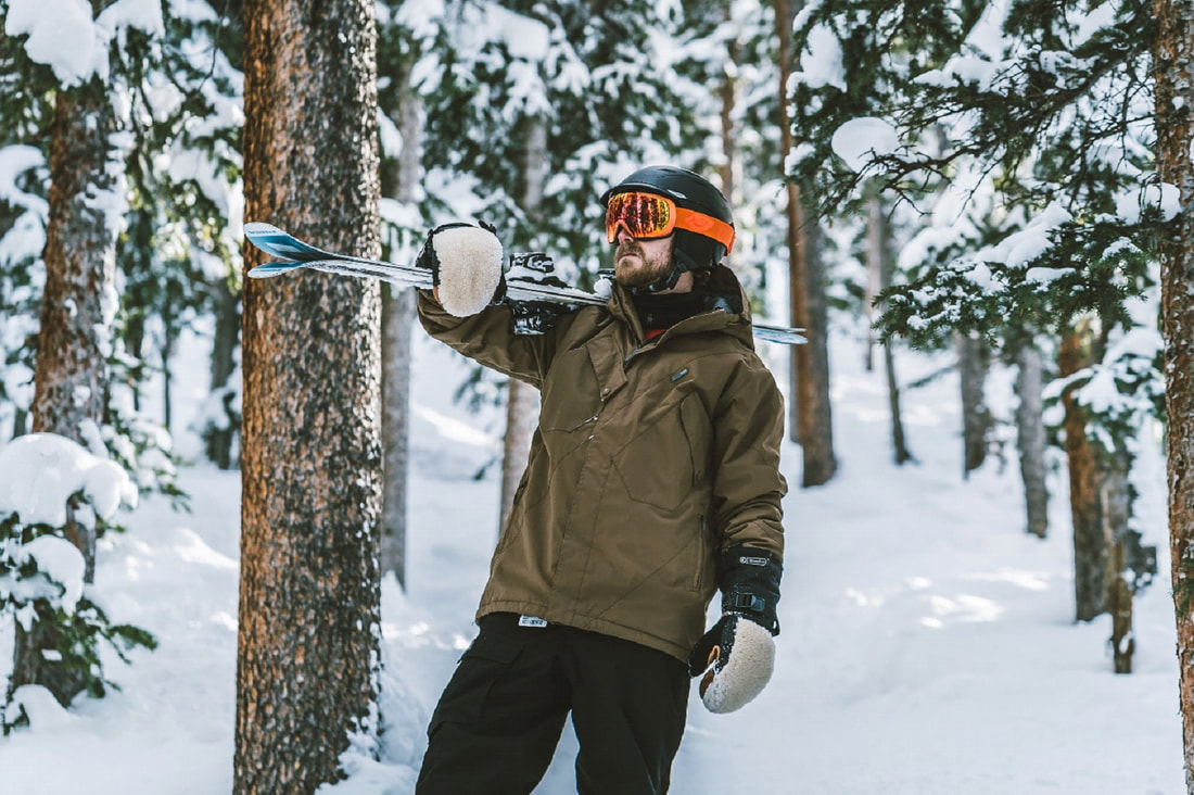 mężczyzna w górach trzyma narty i ma na sobie kurtkę narciarską