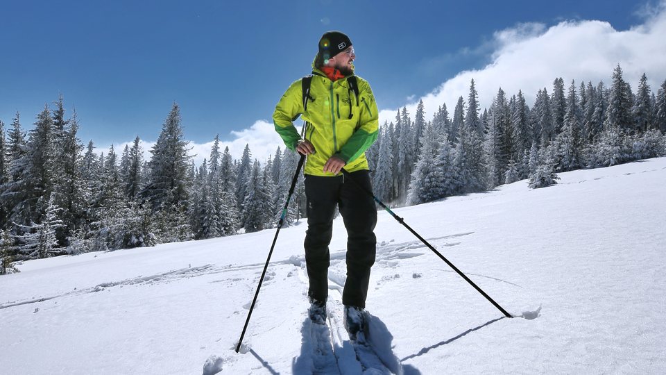 Instruktor skiturowy w limonkowej kurtce stoi na ośnieżonym stoku.
