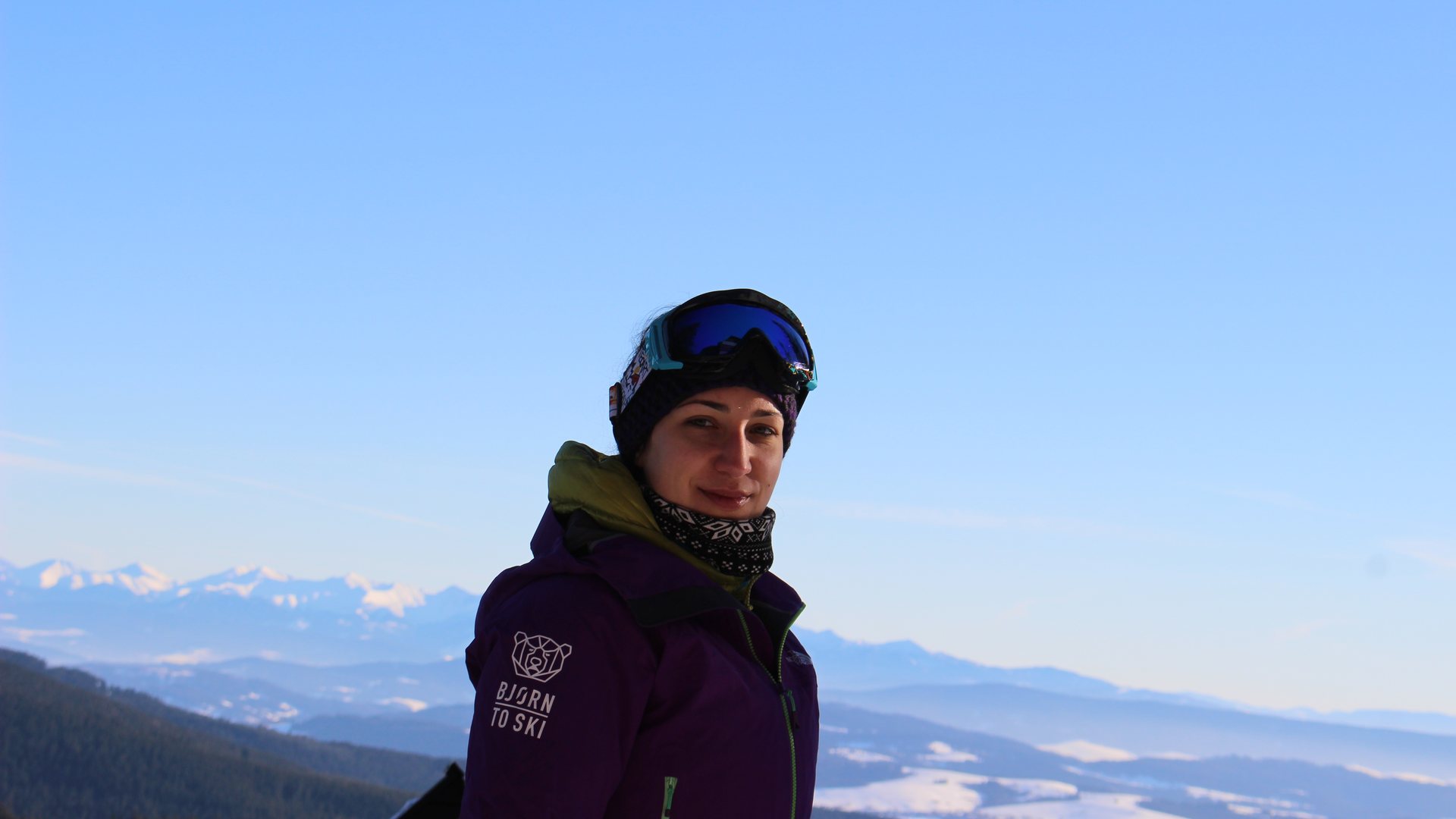 Kobieta w kurtce z logo BJØRN TO SKI na tle zimowej panoramy gór.
