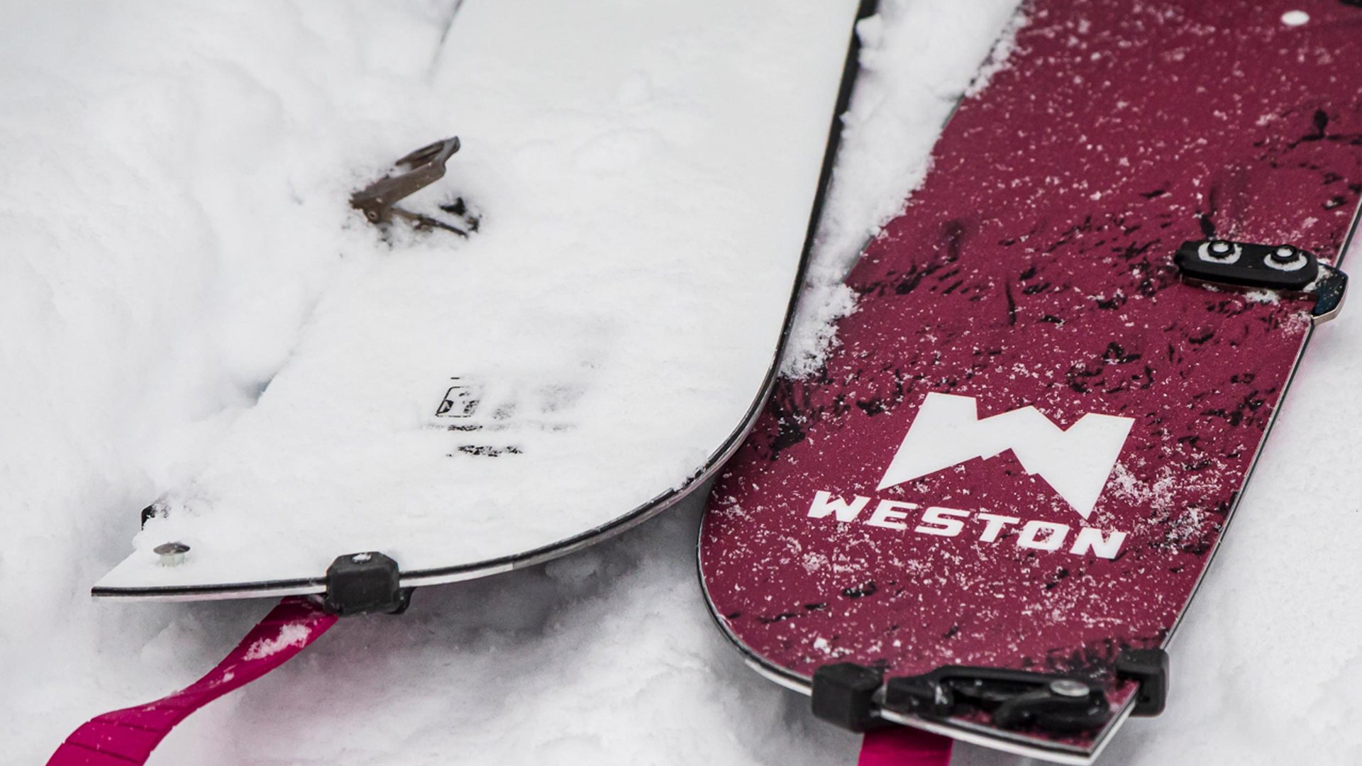 Rozdzielony splitboard leżący na śniegu z widocznymi łączeniami.
