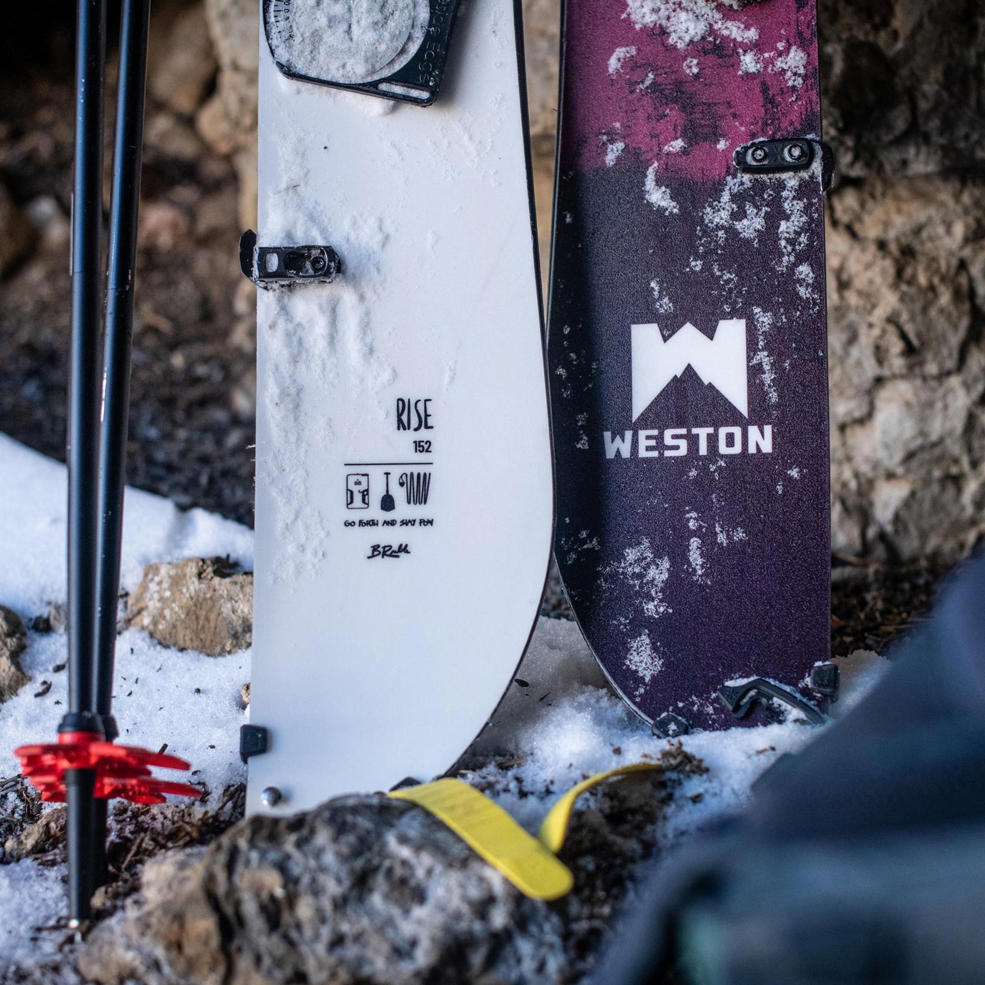 Końce splitboardów Weston Rise ustawionych w śniegu obok kijów.