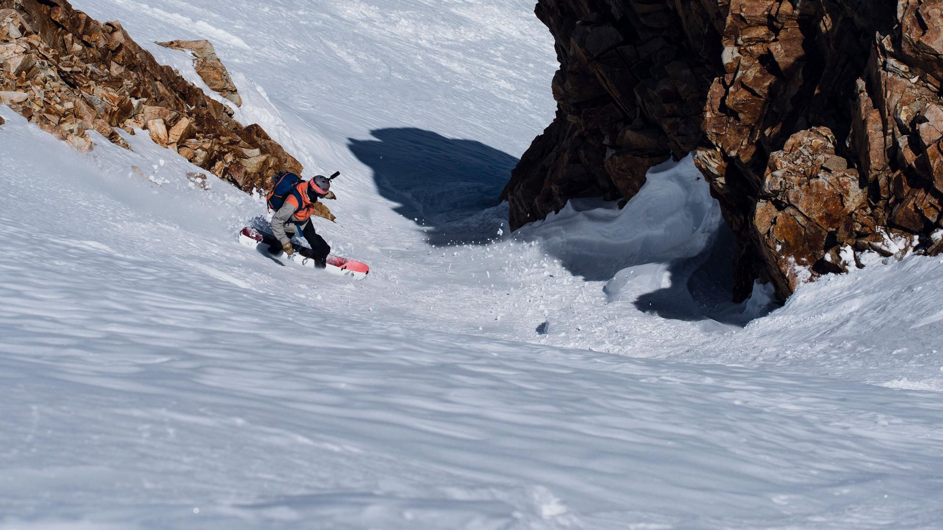 Splitboarder zjeżdża stromym, śnieżnym żlebem w wysokich górach.